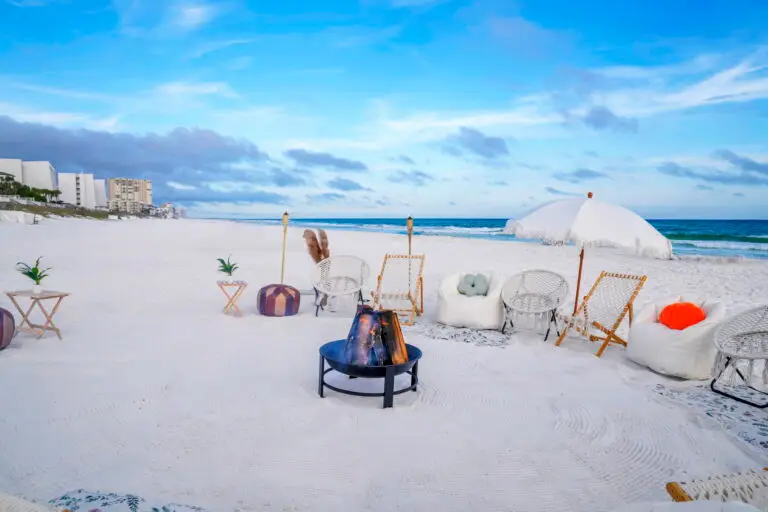 A luxury beachside bonfire in Santa Rosa Beach along 30A with a white umbrella, lounge chairs, bean bags, and a lit fire pit.