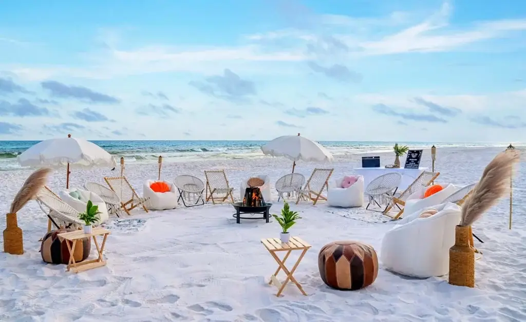 A large luxury beach bonfire setup on 30A with numerous white lounge chairs, umbrellas, and a fire pit near Destin FL.