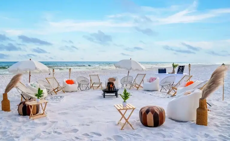 A large luxury beach bonfire setup on 30A with numerous white lounge chairs, umbrellas, and a fire pit near Destin FL.