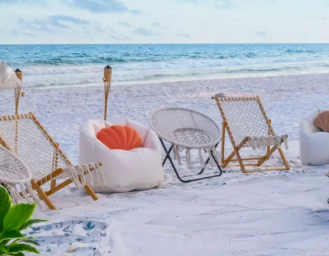 A cozy beachside bonfire in Santa Rosa Beach along 30A with woven chairs, a white beanbag, and a tiki torch on the sand.