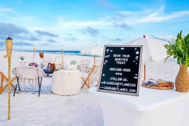 A beachside bonfire booking sign on a table along 30A in Miramar Beach with contact information for Sand & Flames Co.