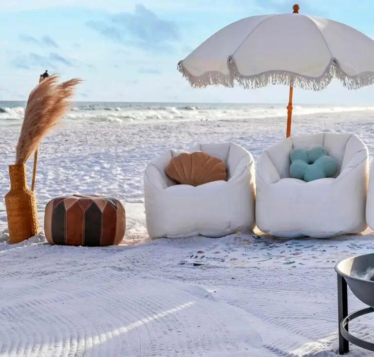 A cozy beachside bonfire setup along 30A with two white bean bag chairs under a fringe beach umbrella in Miramar Beach.